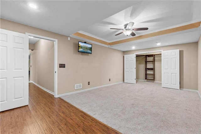 interior space with a raised ceiling, hardwood / wood-style floors, and ceiling fan