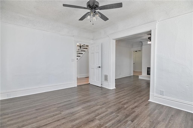 empty room with ceiling fan, a textured ceiling, a brick fireplace, and dark hardwood / wood-style flooring