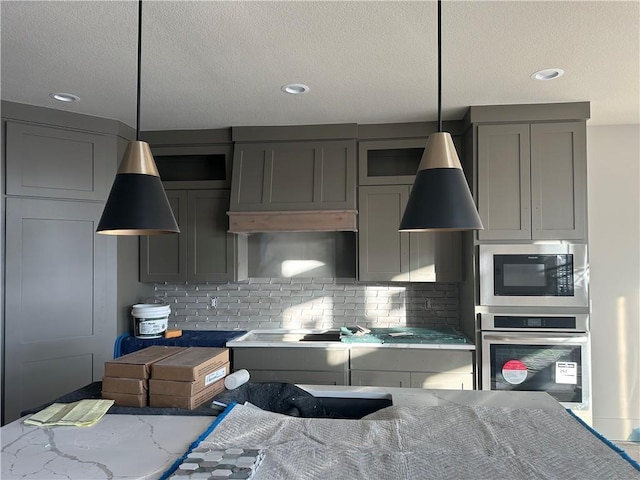 kitchen featuring built in microwave, stainless steel oven, hanging light fixtures, light stone countertops, and decorative backsplash