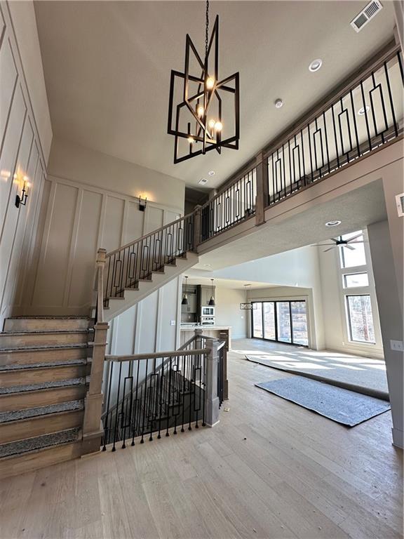 staircase featuring a notable chandelier, wood finished floors, visible vents, and a towering ceiling