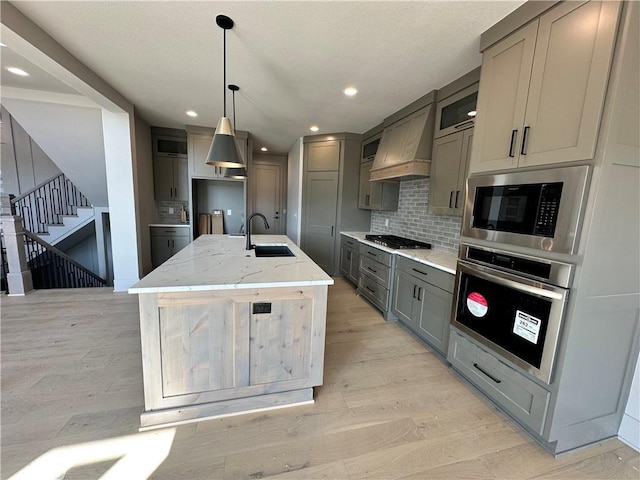 kitchen with gray cabinets, a sink, appliances with stainless steel finishes, decorative backsplash, and custom exhaust hood