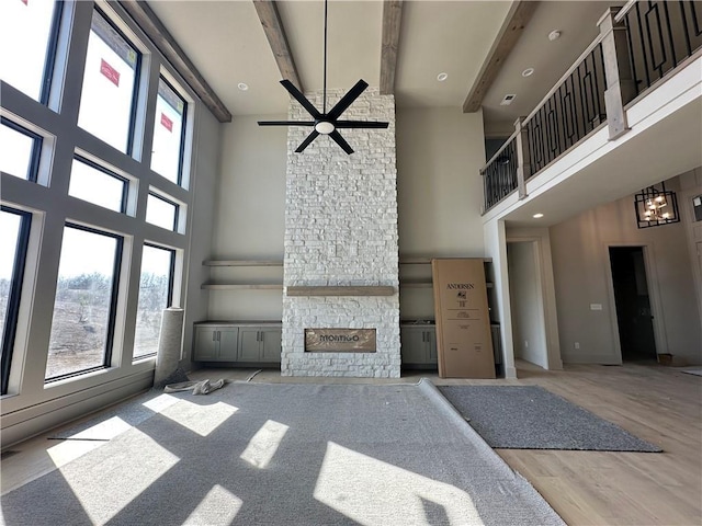 unfurnished living room featuring ceiling fan, beamed ceiling, a stone fireplace, and wood finished floors