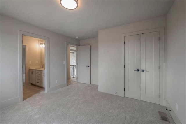 unfurnished bedroom with baseboards, visible vents, light colored carpet, a closet, and connected bathroom