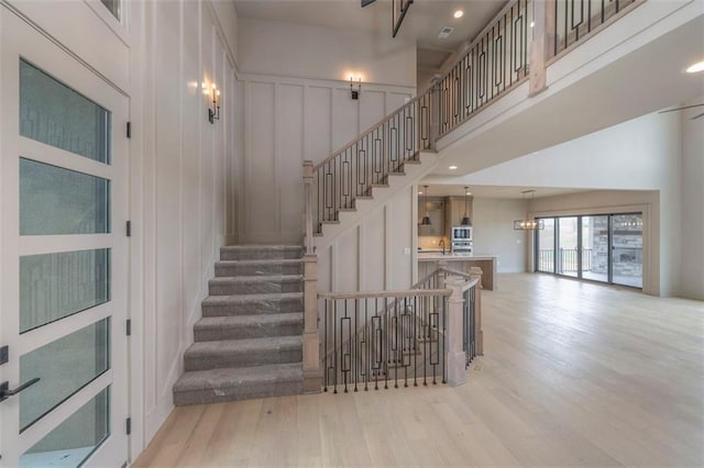 staircase with wood finished floors, a decorative wall, and a towering ceiling