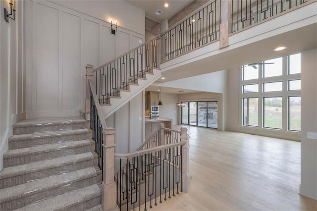 stairs featuring wood finished floors, a high ceiling, recessed lighting, and a decorative wall