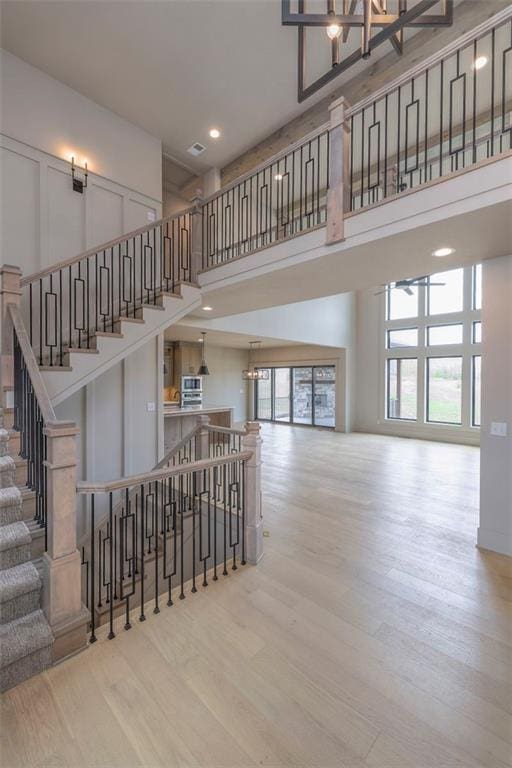 stairs featuring recessed lighting, a towering ceiling, wood finished floors, visible vents, and a chandelier