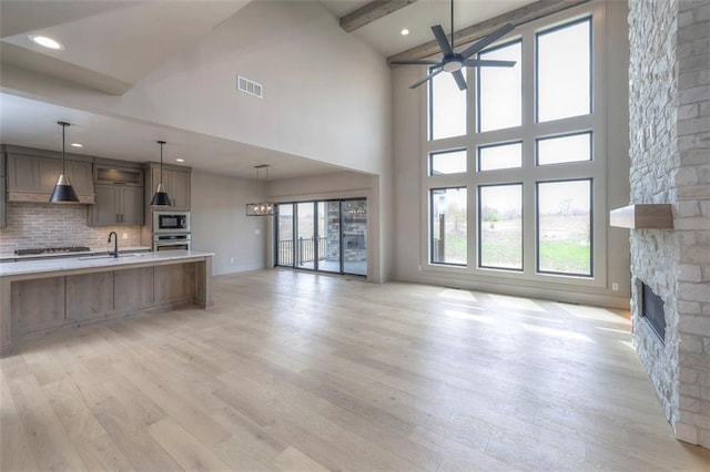 unfurnished living room with light wood-style floors, a stone fireplace, visible vents, and ceiling fan