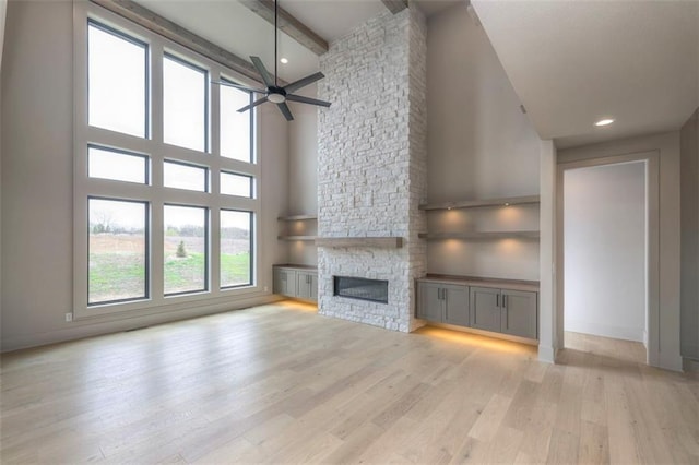 unfurnished living room featuring high vaulted ceiling, a ceiling fan, beamed ceiling, light wood finished floors, and a fireplace