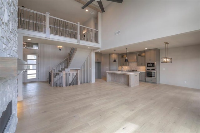 unfurnished living room with light wood-type flooring, a stone fireplace, visible vents, and high vaulted ceiling