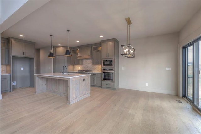 kitchen with a sink, light wood-style floors, gray cabinetry, appliances with stainless steel finishes, and premium range hood