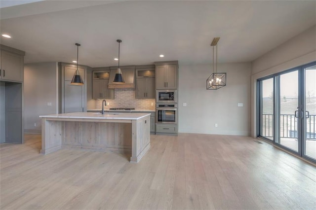 kitchen featuring light wood finished floors, stainless steel appliances, a sink, baseboards, and gray cabinets