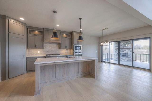 kitchen featuring light wood finished floors, a sink, tasteful backsplash, gray cabinets, and appliances with stainless steel finishes