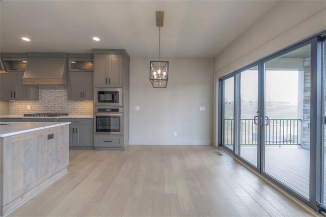 kitchen featuring gray cabinets, premium range hood, light wood-type flooring, a chandelier, and appliances with stainless steel finishes