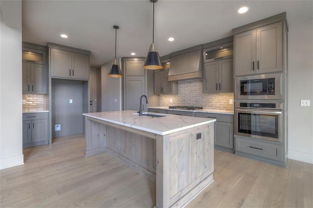 kitchen with a sink, custom range hood, backsplash, appliances with stainless steel finishes, and gray cabinetry