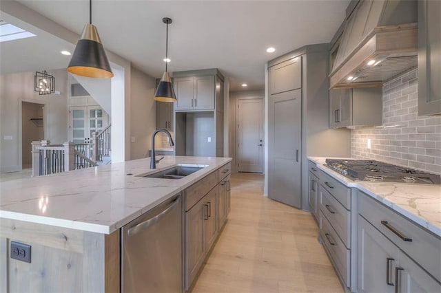 kitchen with gray cabinets, a sink, a center island with sink, appliances with stainless steel finishes, and custom exhaust hood