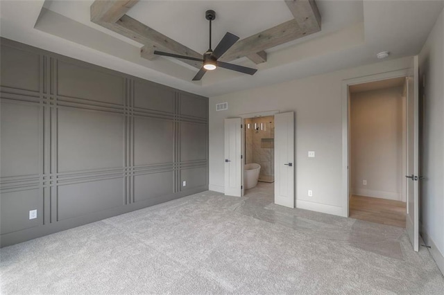 unfurnished bedroom featuring a tray ceiling, visible vents, a ceiling fan, ensuite bath, and carpet flooring
