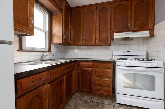 kitchen featuring light tile patterned flooring, sink, white gas range oven, and tasteful backsplash