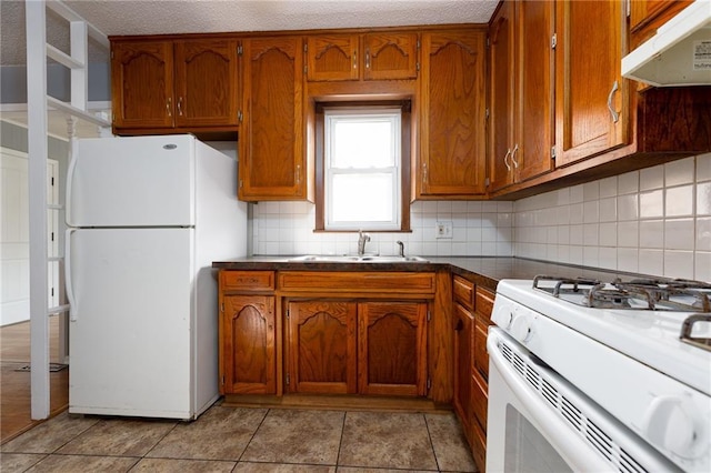 kitchen with sink, a textured ceiling, light tile patterned floors, white appliances, and backsplash