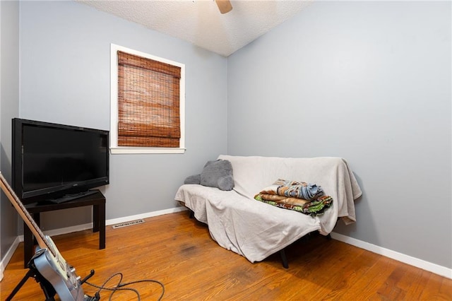 sitting room featuring wood-type flooring, ceiling fan, and a textured ceiling