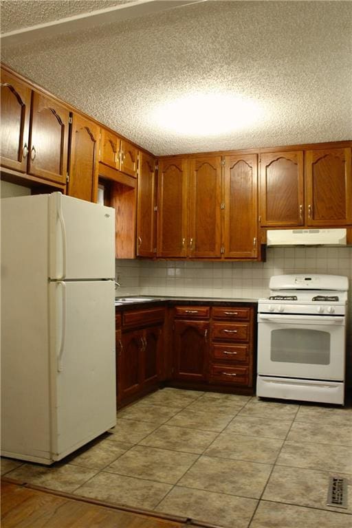 kitchen featuring backsplash, white appliances, light tile patterned floors, and a textured ceiling