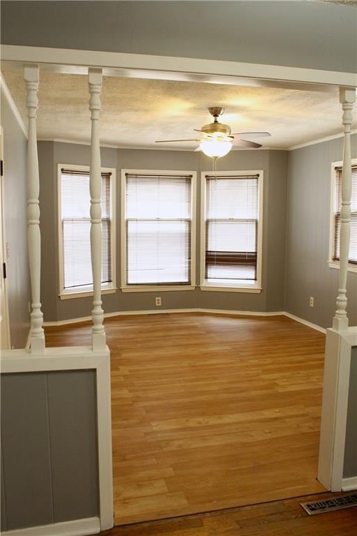 interior space with hardwood / wood-style flooring, ornamental molding, ceiling fan, and ornate columns