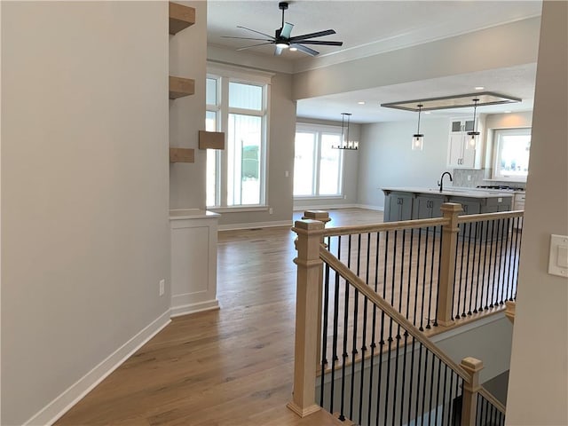 hall with an upstairs landing, a sink, light wood-style flooring, and baseboards