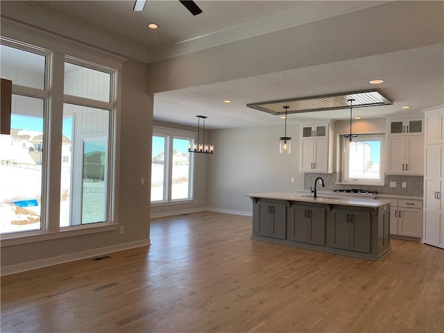 kitchen featuring light countertops, an island with sink, glass insert cabinets, and white cabinetry