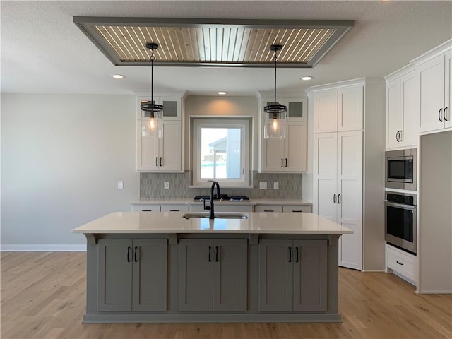 kitchen featuring stainless steel appliances, light countertops, pendant lighting, and a kitchen island with sink