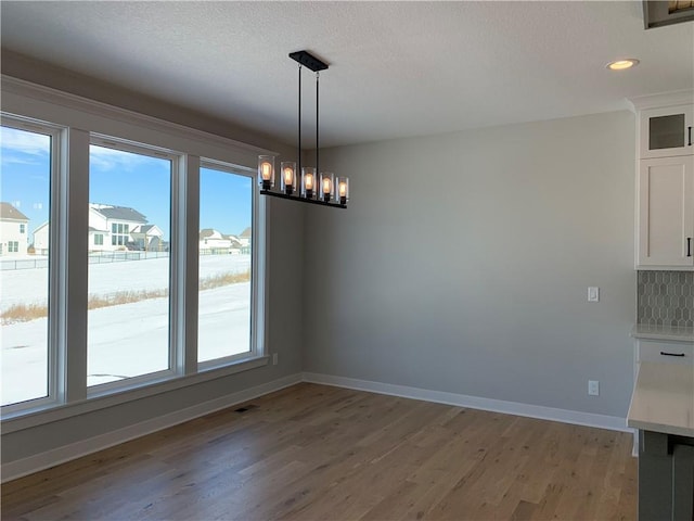 unfurnished dining area featuring a chandelier, light wood-style floors, and baseboards