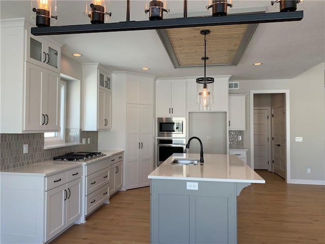 kitchen featuring decorative light fixtures, a center island with sink, stainless steel appliances, light countertops, and white cabinetry