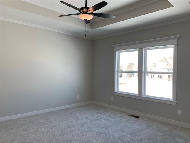 carpeted empty room featuring ceiling fan, visible vents, baseboards, ornamental molding, and a tray ceiling