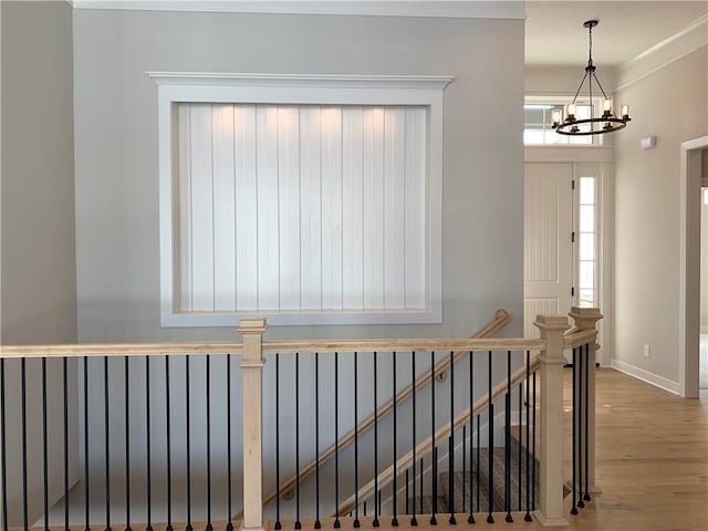 hallway featuring baseboards, wood finished floors, an upstairs landing, and an inviting chandelier