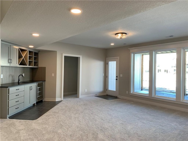 kitchen with open shelves, a sink, baseboards, dark colored carpet, and dark countertops