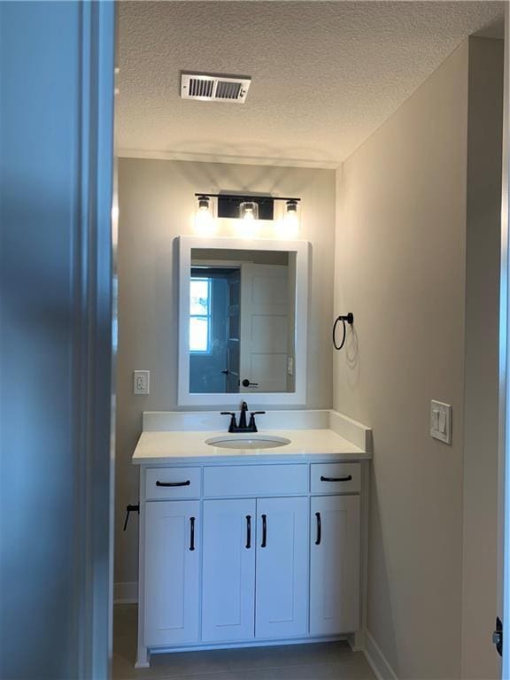 bathroom featuring baseboards, visible vents, a textured ceiling, and vanity