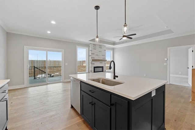 kitchen with an island with sink, light hardwood / wood-style floors, sink, dishwasher, and a raised ceiling