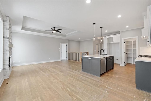 kitchen with white cabinetry, a center island with sink, hanging light fixtures, a tray ceiling, and stainless steel dishwasher