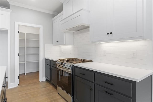 kitchen featuring light hardwood / wood-style flooring, custom range hood, stainless steel gas range oven, white cabinets, and decorative backsplash