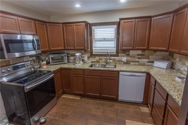 kitchen with dark hardwood / wood-style floors, sink, stainless steel appliances, backsplash, and light stone countertops