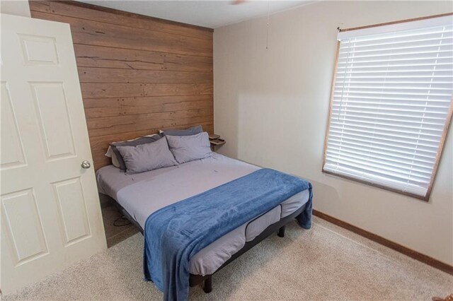 bedroom with wooden walls and light carpet