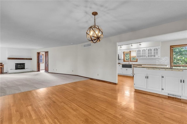 unfurnished living room with light carpet, a brick fireplace, a chandelier, and sink