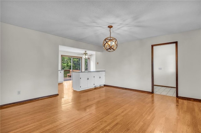 unfurnished room featuring ceiling fan with notable chandelier, light hardwood / wood-style floors, and a textured ceiling