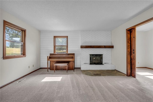 unfurnished living room featuring a textured ceiling, plenty of natural light, a brick fireplace, and carpet flooring