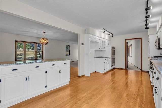 kitchen with light wood-type flooring, track lighting, decorative light fixtures, appliances with stainless steel finishes, and white cabinets