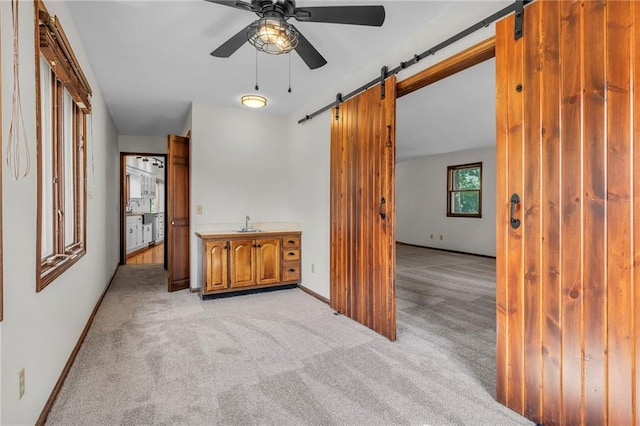 carpeted spare room with a barn door, ceiling fan, and sink