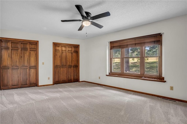 unfurnished bedroom featuring a textured ceiling, light colored carpet, ceiling fan, and multiple closets