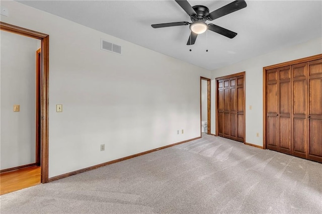 unfurnished bedroom featuring multiple closets, light colored carpet, and ceiling fan