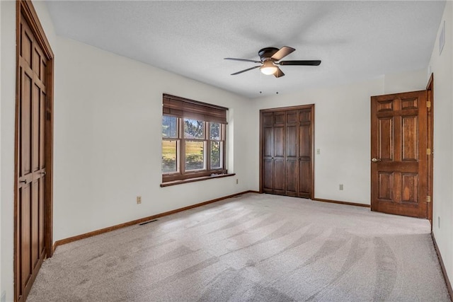 unfurnished bedroom with light colored carpet, two closets, ceiling fan, and a textured ceiling