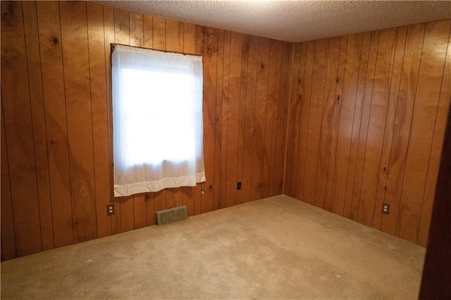 carpeted spare room featuring a textured ceiling and wooden walls