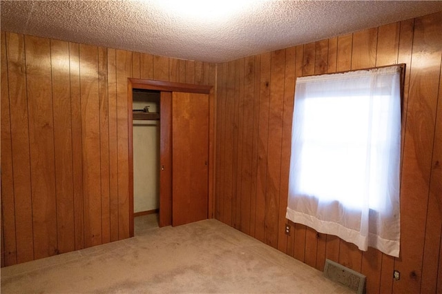 unfurnished bedroom featuring a textured ceiling, carpet flooring, wood walls, and a closet