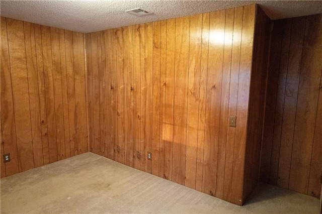 unfurnished room with a textured ceiling, carpet, and wooden walls